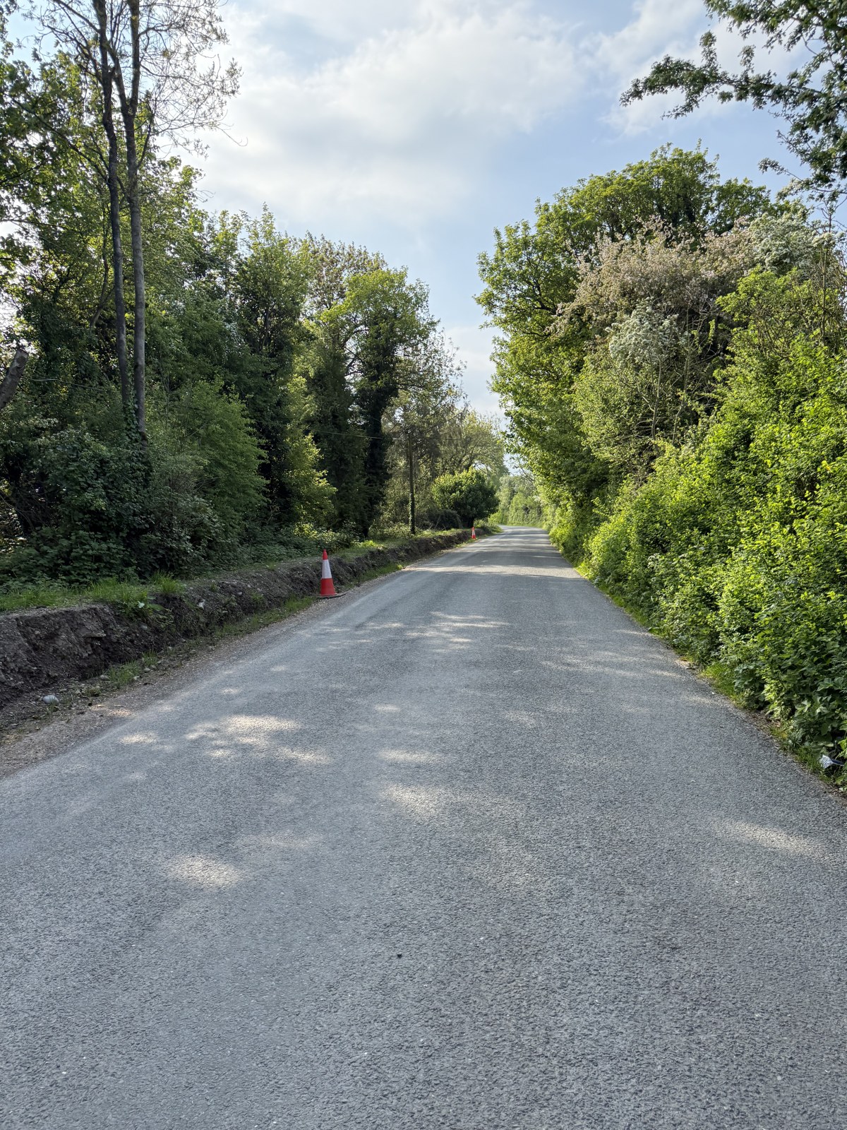 The same approach lane on 1 May 2025, a clay bank in place along the left, the growth cut back and the road resurfaced