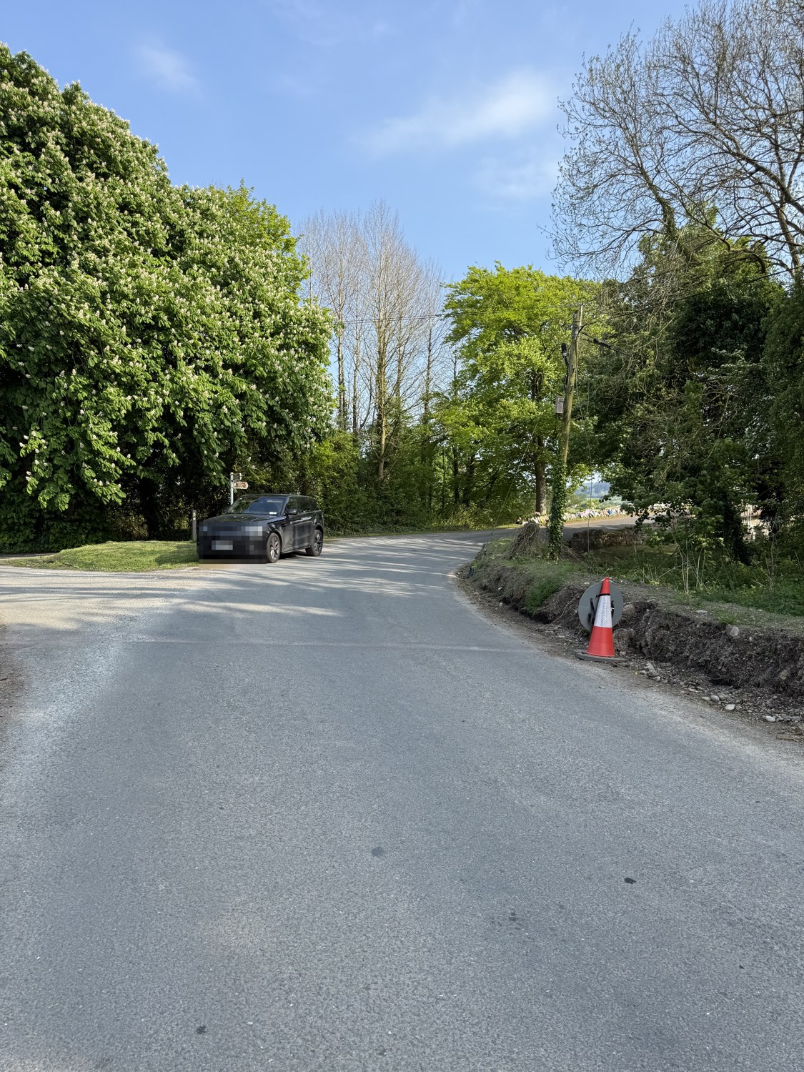 The same turn on 1 May 2025, a cut clay bank along the right edge with clay and stones at the road edge, the bridge parapet beyond